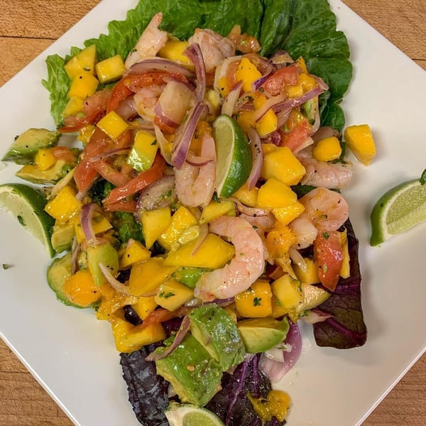 Shrimp ceviche with mango, avocado, red onion, and lime on a bed of lettuce.