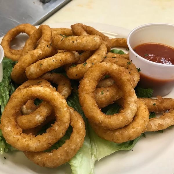 Golden-brown fried calamari rings on a bed of lettuce with a side of marinara sauce.