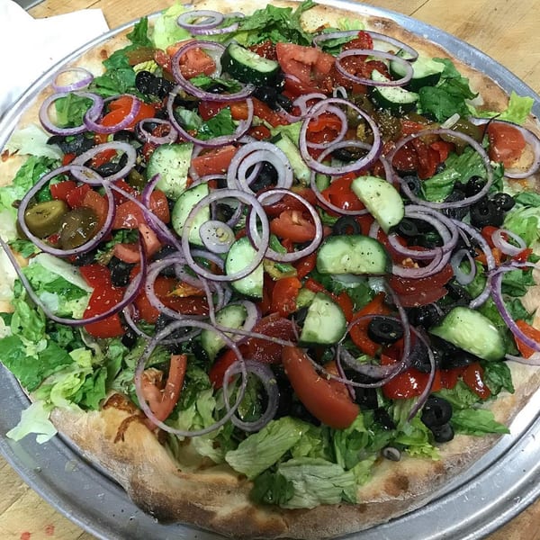 Tony's Pizza salad pizza, topped with fresh lettuce, tomatoes, cucumbers, red onions, and black olives.